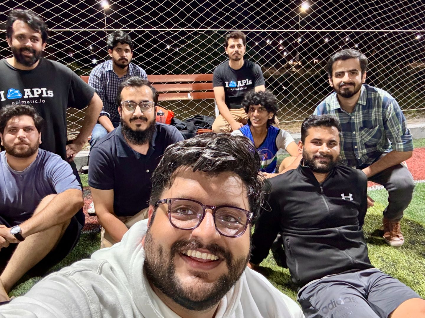 Ten of the APIMatic team on a floodlit five-a-side pitch at night, some in APIMatic shirts